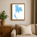 Framed map of Thailand on a wall above a beige sofa with a plant beside it.
