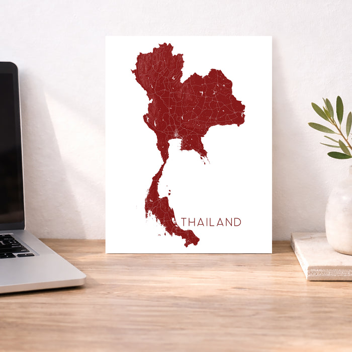 Map of Thailand on a white background next to a laptop on a wooden desk.