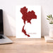 Map of Thailand on a white background next to a laptop on a wooden desk.