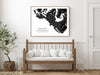 Framed black and white map of Tofino on a wall above a wooden bench with white cushions.