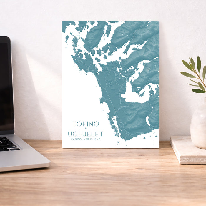 Map of Tofino and Ucluelet on Vancouver Island displayed on a desk with a laptop and plant.