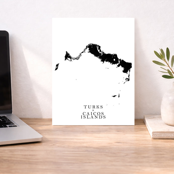 Map of Turks and Caicos Islands on a white background next to a laptop on a wooden desk.
