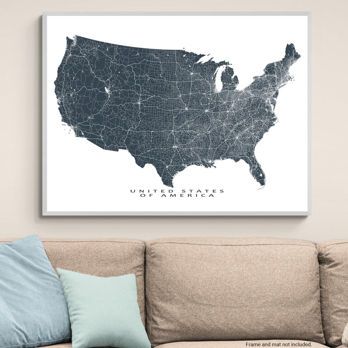 Framed map of the United States on a wall above a beige sofa with light blue pillows.