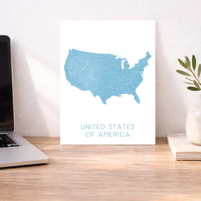 Map of the United States on a white background next to a laptop on a wooden desk.
