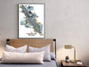 Framed map of Vancouver Island above a bed with pillows and a lamp.