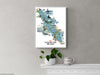 Framed map of Vancouver Island on a gray wall with a plant and mug below.