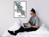 Person sitting on a bed using a laptop with a map of Vancouver Island on the wall.