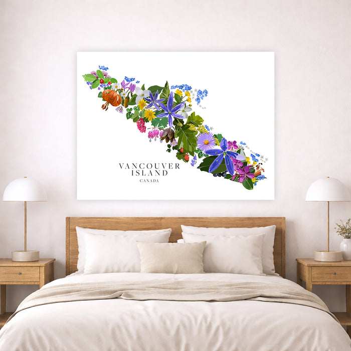 A large rectangular wall art print showing a colorful floral map of Vancouver Island, Canada, displayed above a neatly made bed in a bright bedroom. The artwork features many flowers in purple, blue, pink, yellow, orange, and green on a white background, with the text 'VANCOUVER ISLAND CANADA' below.