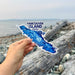 Hand holding a Vancouver Island, Canada sticker with a beach background