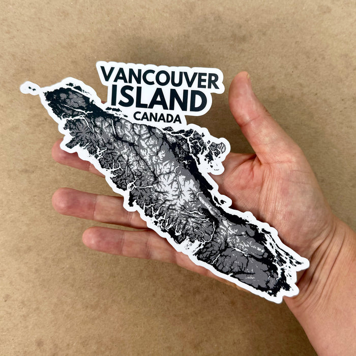 Hand holding a sticker of Vancouver Island, Canada on a brown background