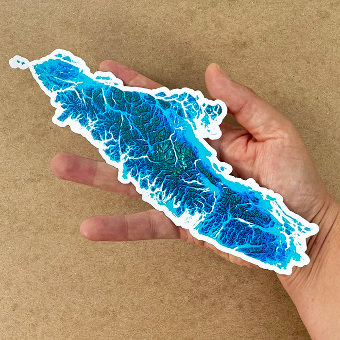 Hand holding a blue and white Vancouver Island map design on a brown background