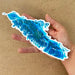Hand holding a blue and white Vancouver Island map design on a brown background