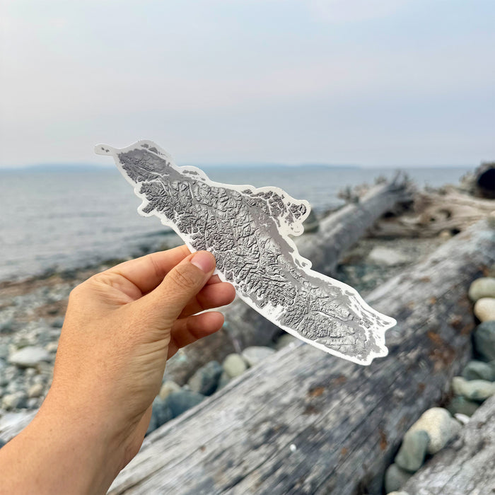 Hand holding a detailed map of Vancouver Island BC against a beach background