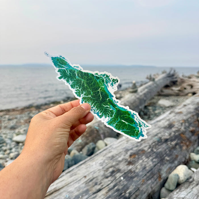 Hand holding a green island-shaped sticker with a beach and ocean in the background