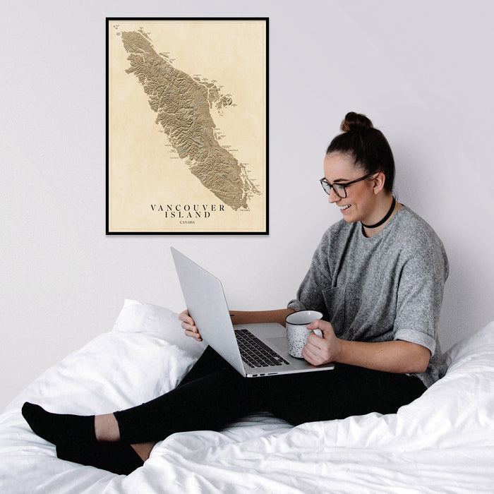 Person sitting on a bed using a laptop with a framed map of Vancouver Island on the wall.