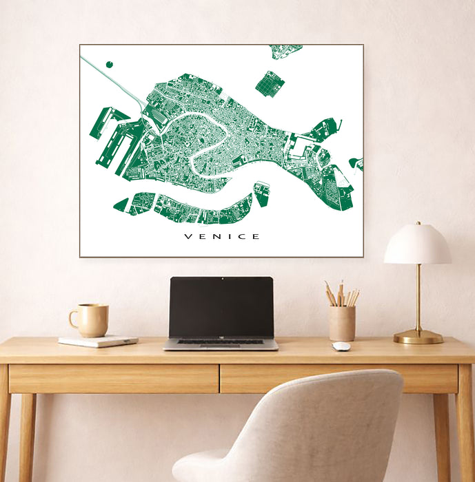 Framed map of Venice on a wall above a desk with a laptop and lamp.