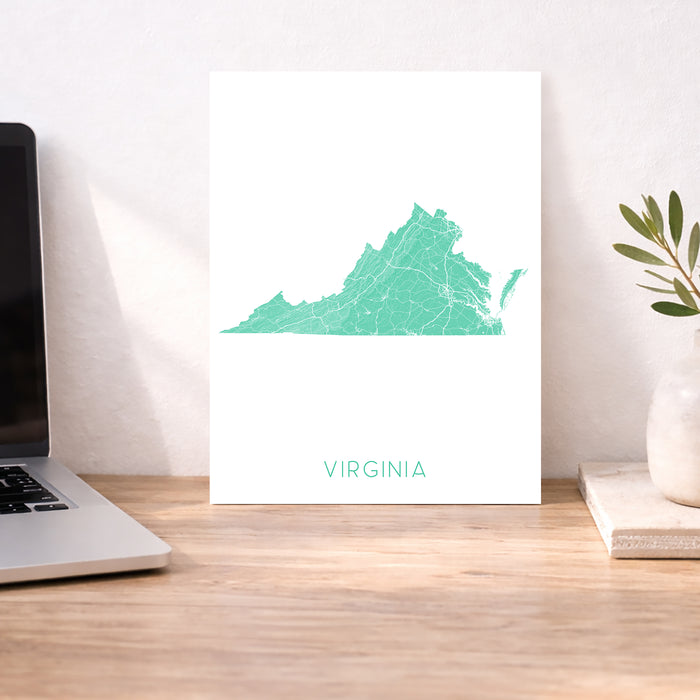 Map of Virginia on a white background next to a laptop on a wooden desk.