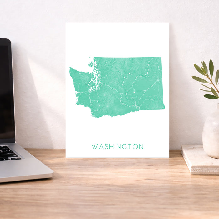 Map of Washington on a white background next to a laptop on a wooden desk.