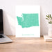 Map of Washington on a white background next to a laptop on a wooden desk.