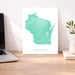 Map of Wisconsin on a white background next to a laptop on a wooden desk.