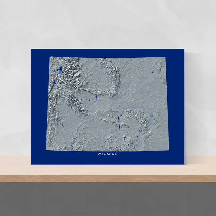 Wyoming state map print with natural landscape in greyscale and a navy blue background designed by Maps As Art.